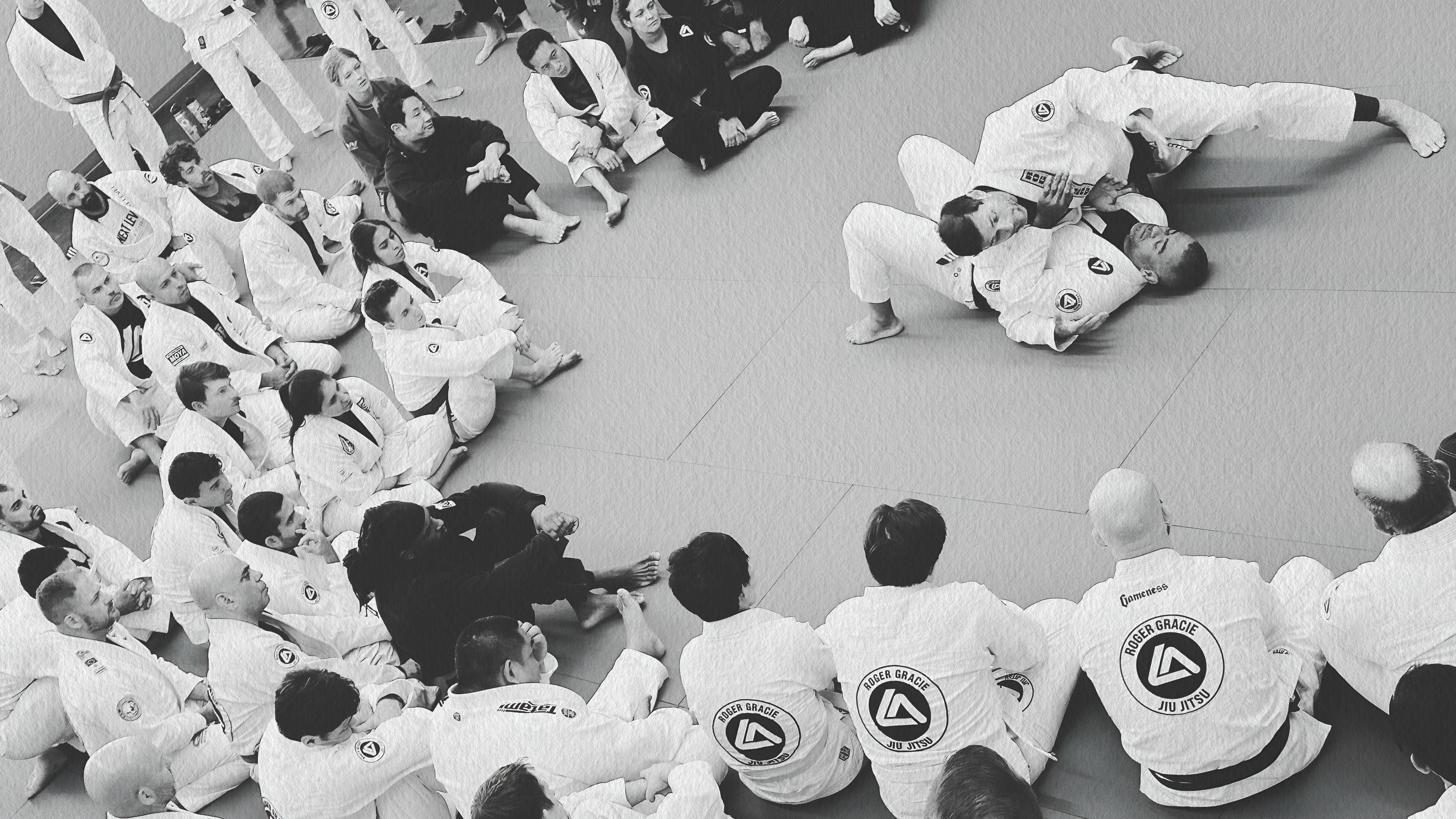Students seated around the mat watching a technique demonstration